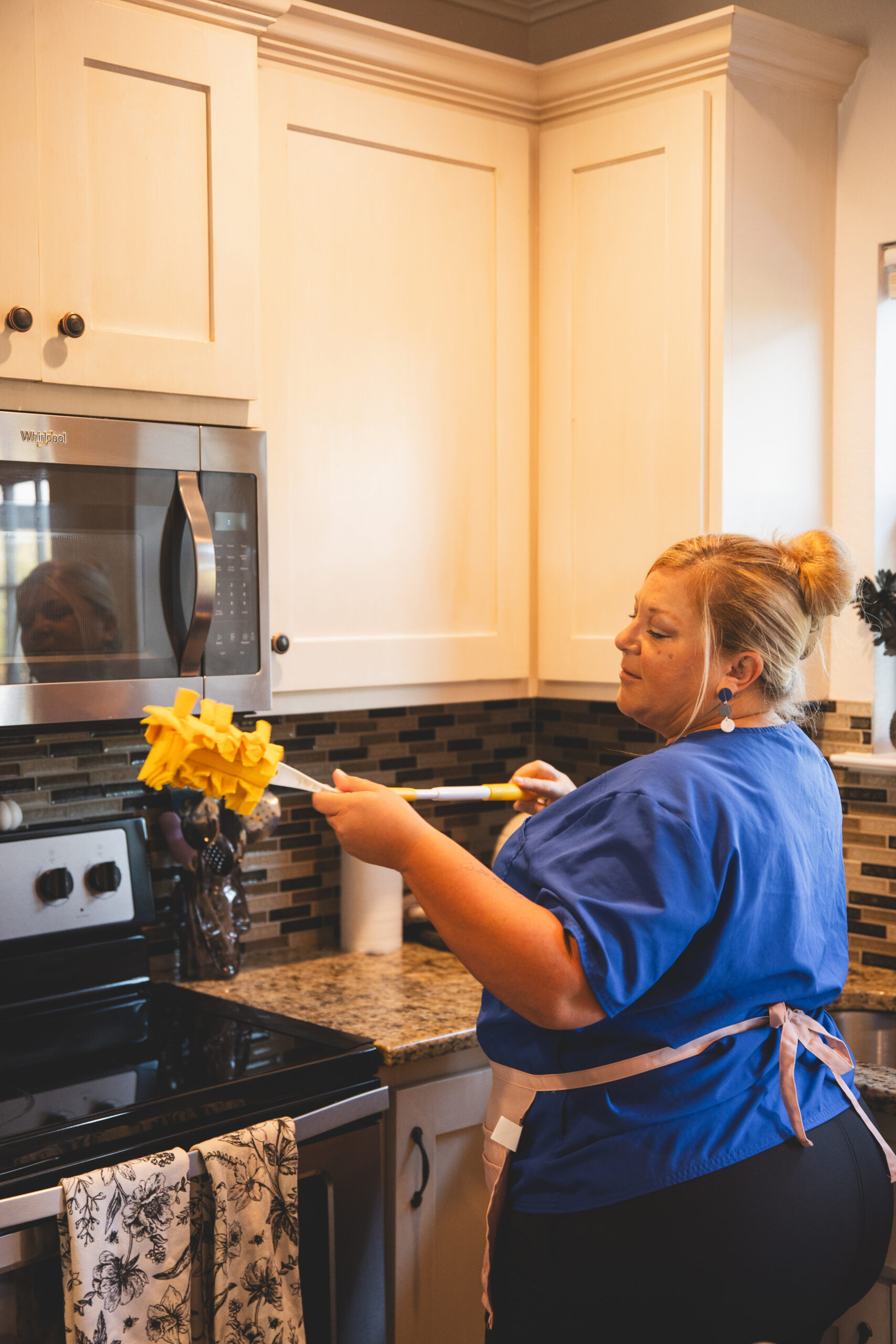 A professional cleaner from The Mop & Broom dusting kitchen cabinets in Benbrook