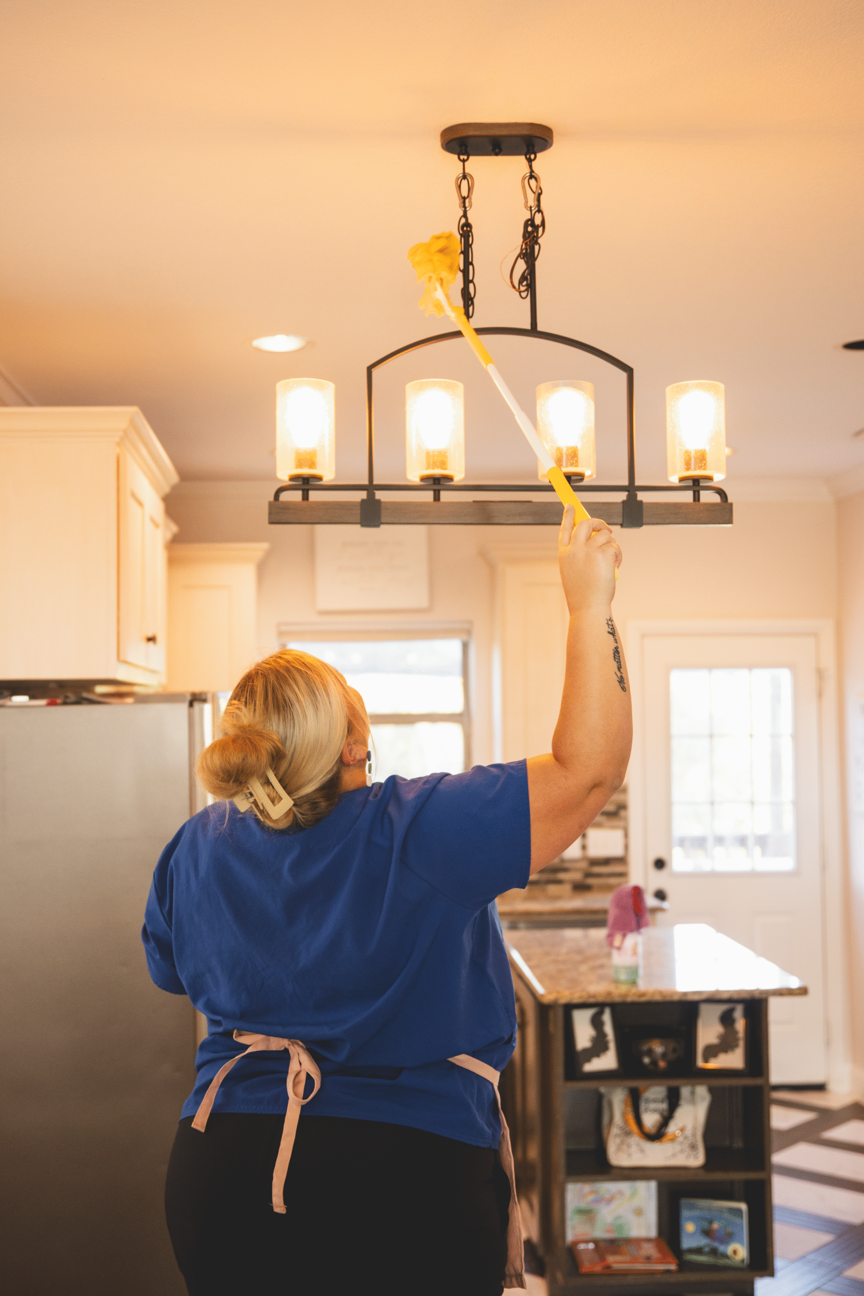 A cleaner from The Mop & Broom dusting a hanging light fixture in a Crowley home